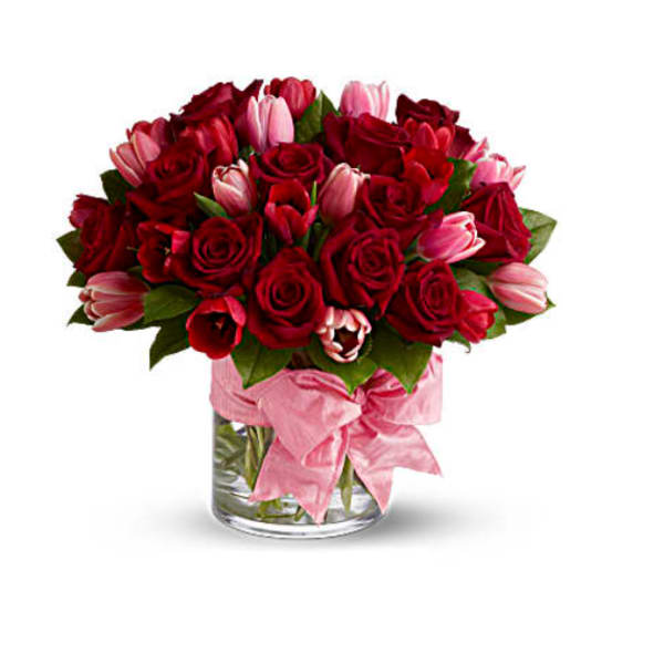 Bouquet of red roses and pink tulips in a glass vase with a pink ribbon