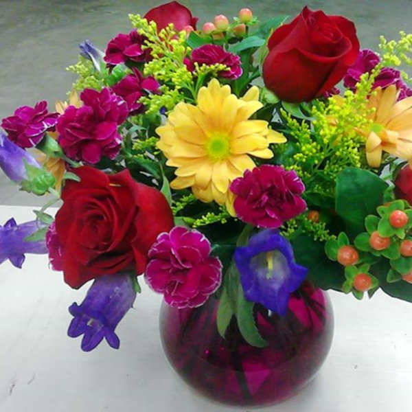 Mixed bouquet in a purple glass vase with red roses and yellow daisies