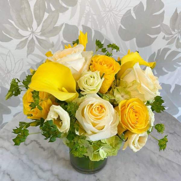 Yellow and white roses with yellow calla lilies in a glass vase