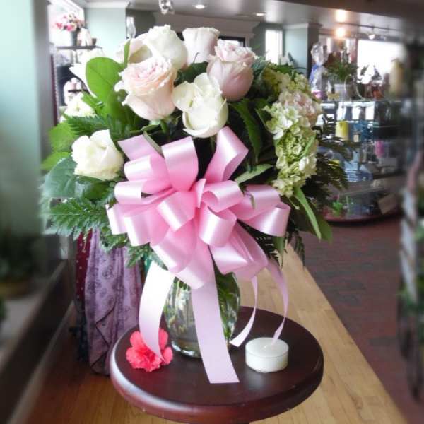 Pink and white rose bouquet in a glass vase with a large pink ribbon