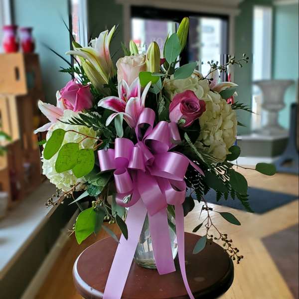 Bouquet of pink lilies, roses, and hydrangeas in a glass vase with a pink ribbon