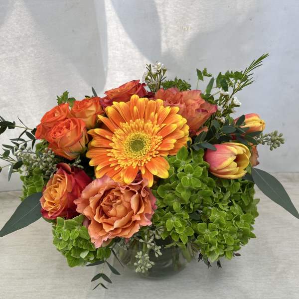 Orange gerbera and roses in a glass vase with green hydrangea