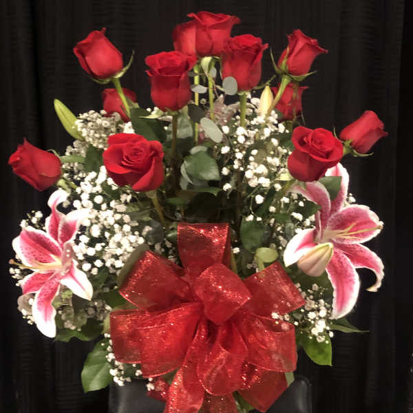 Red roses and pink lilies arranged in a glass vase with a red bow.