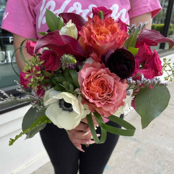 Handheld bouquet of pink, coral, and white flowers