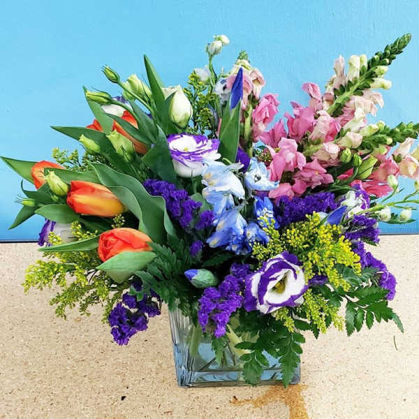 Mixed bouquet in a clear glass vase with pink, purple, blue, and orange flowers