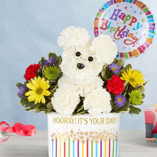 White teddy bear floral arrangement with a birthday balloon in a decorated container