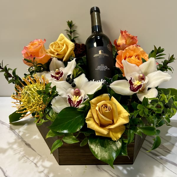 Flower arrangement with roses, orchids, and a wine bottle in a wooden box