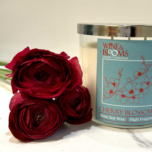 Red roses beside a cherry blossom candle in a glass jar
