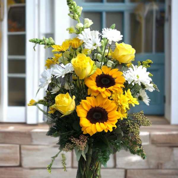 Yellow roses and sunflowers in a clear glass vase with white daisies