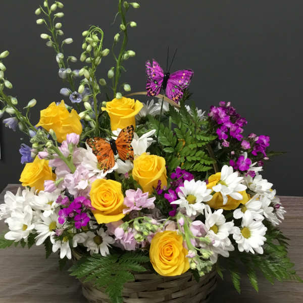 Basket arrangement of yellow roses, white daisies, and purple flowers with butterfly picks