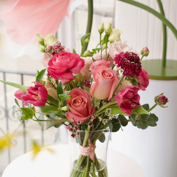 Pink and coral bouquet of roses and tulips in a clear glass vase