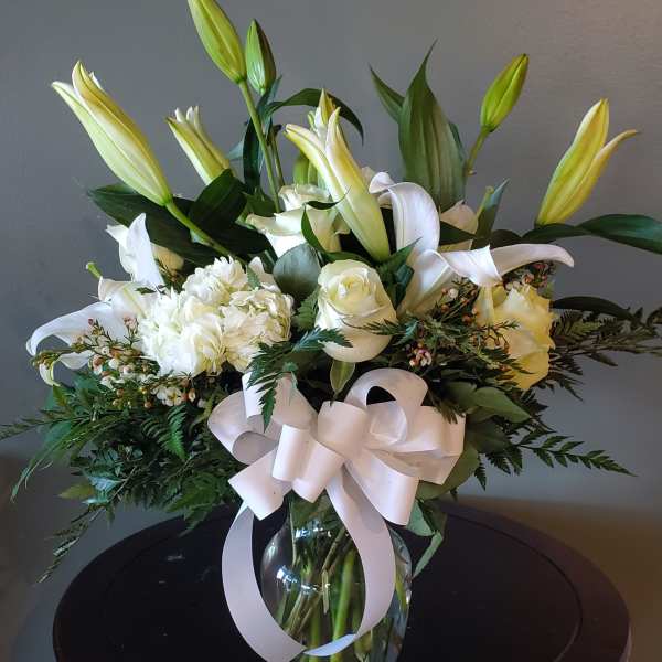 White lilies and roses arranged in a glass vase with a white ribbon