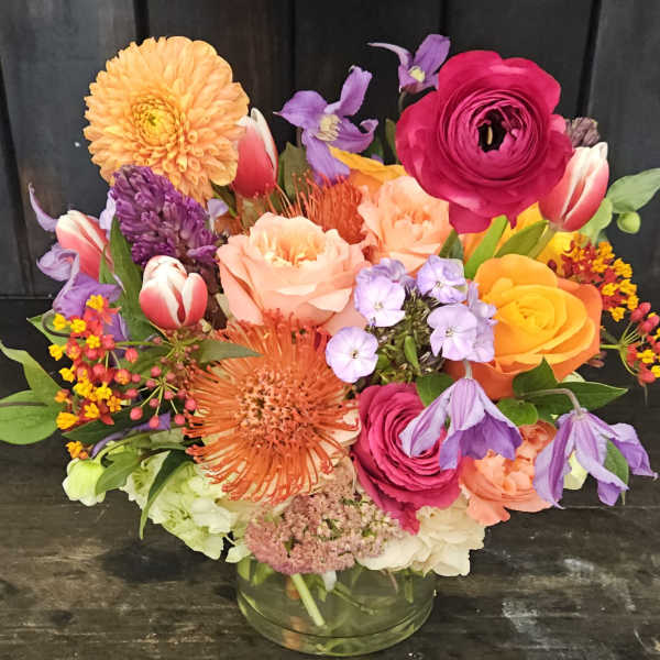 Colorful mixed bouquet in a clear glass vase with roses, tulips, and dahlias