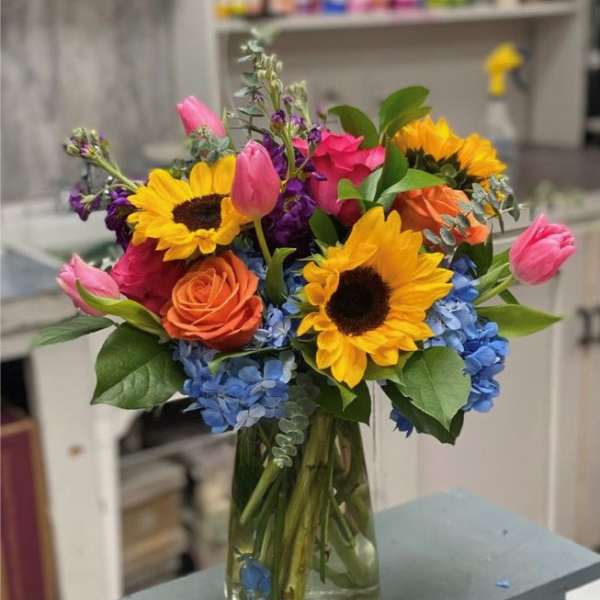 Colorful bouquet of sunflowers, roses, tulips, and hydrangeas in a glass vase