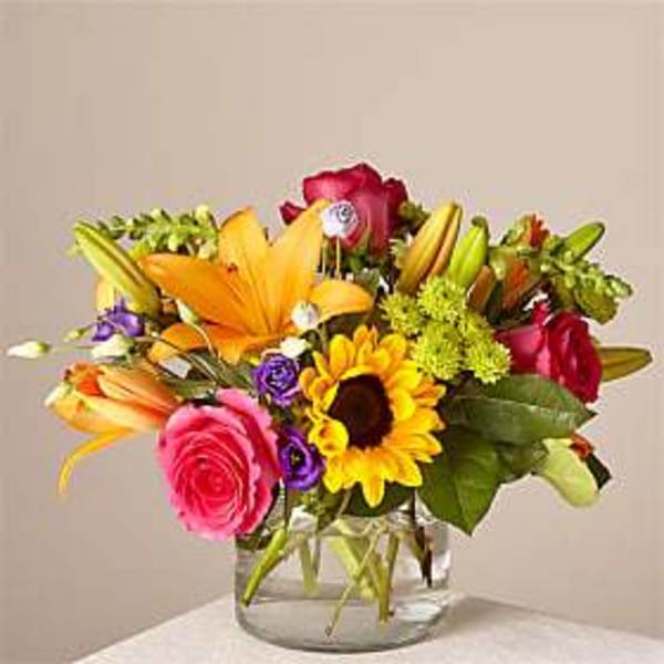 Mixed bouquet of lilies, roses, and a sunflower in a clear glass vase