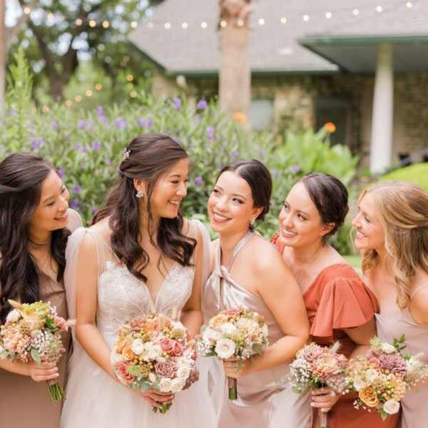 Bride and bridesmaids holding pastel flower bouquets outdoors