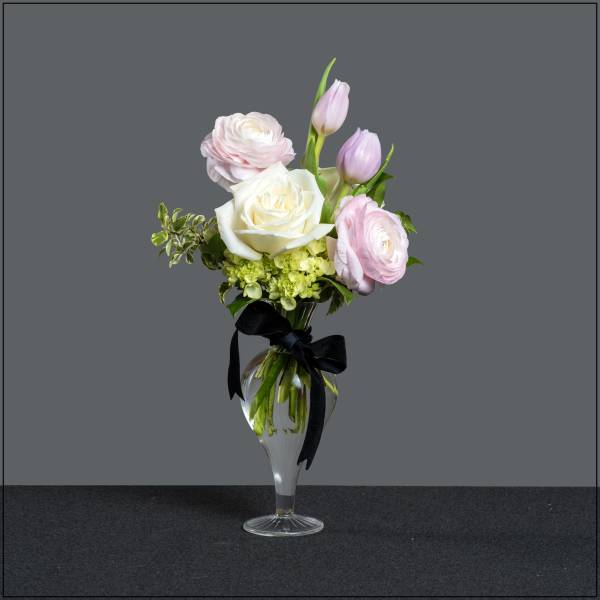 Pink and white flowers arranged in a clear glass vase with a black ribbon