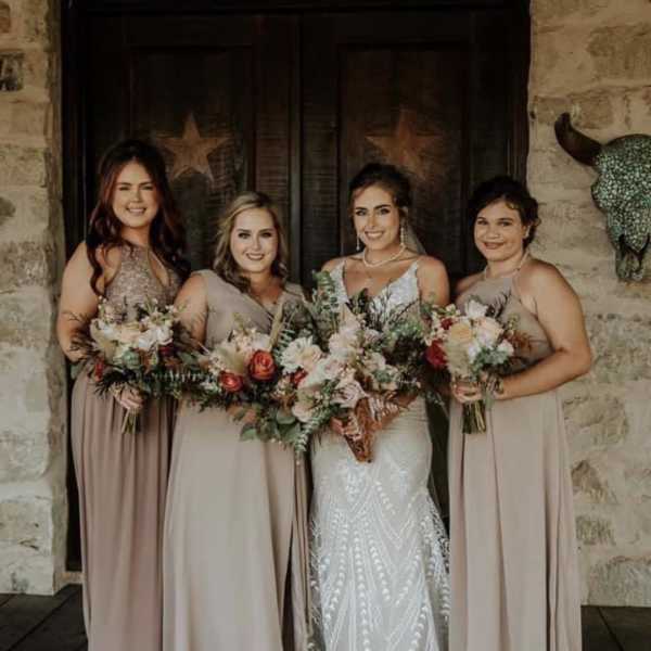 Bride and three bridesmaids holding mixed bouquets in front of a rustic doorway