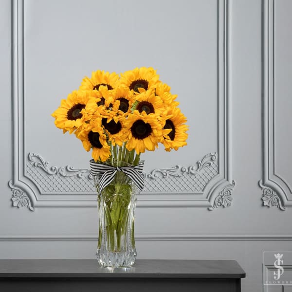 Bouquet of yellow sunflowers in a clear glass vase with a striped ribbon