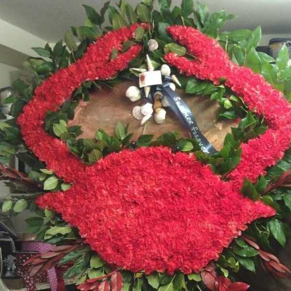 Large red floral funeral wreath with a ribbon and greenery
