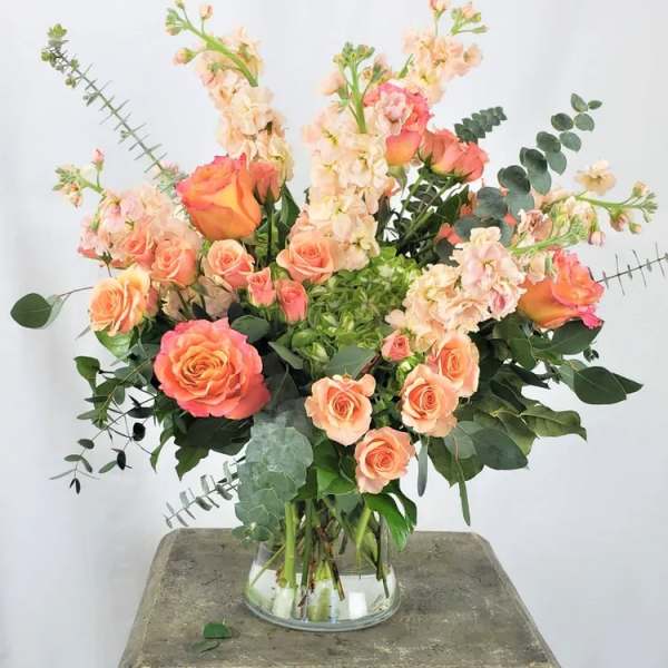 Peach and coral roses with pale pink stock in a clear glass vase