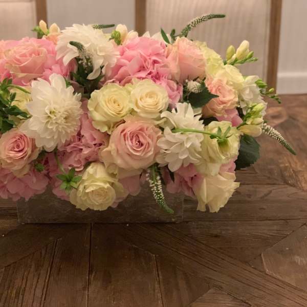 Low floral arrangement of pink and white roses in a clear rectangular vase