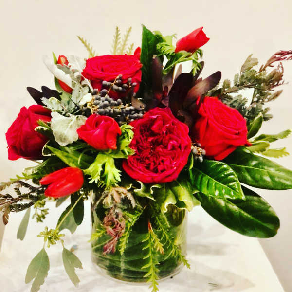 Red roses and mixed greenery arranged in a clear glass vase