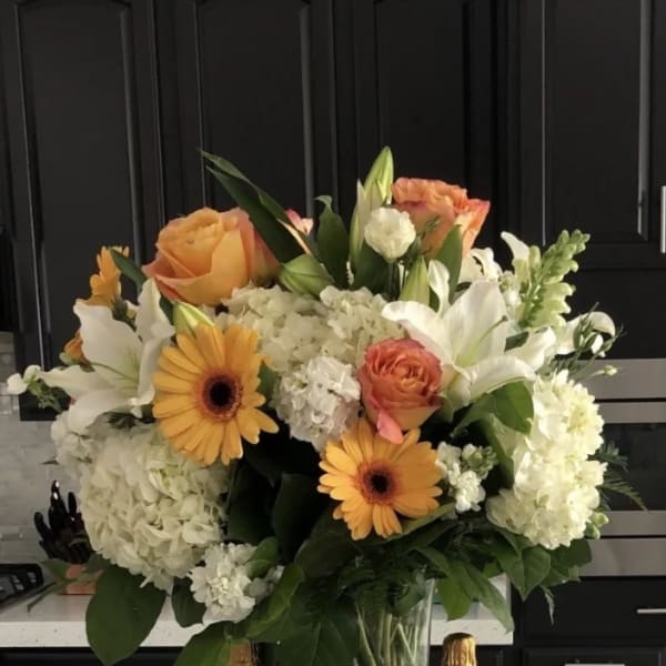 Bouquet of white lilies, peach roses, and yellow gerbera daisies in a glass vase
