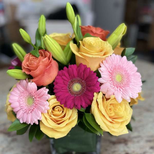 Mixed bouquet of roses, gerbera daisies, and lilies in a glass vase