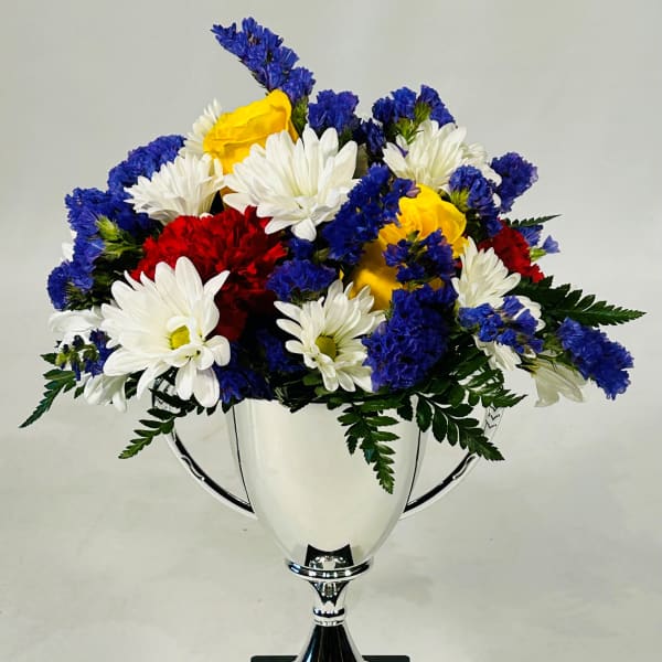 Mixed bouquet of white, yellow, red, and blue flowers in a silver trophy vase