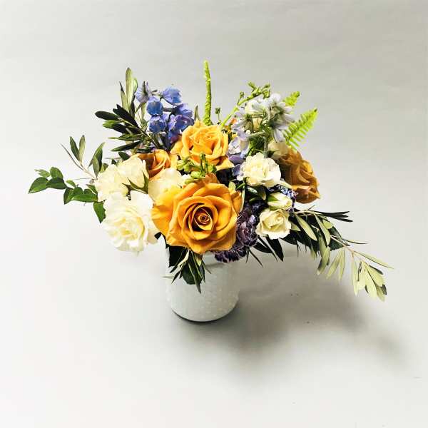 Mixed bouquet of orange, white, and blue flowers in a white vase