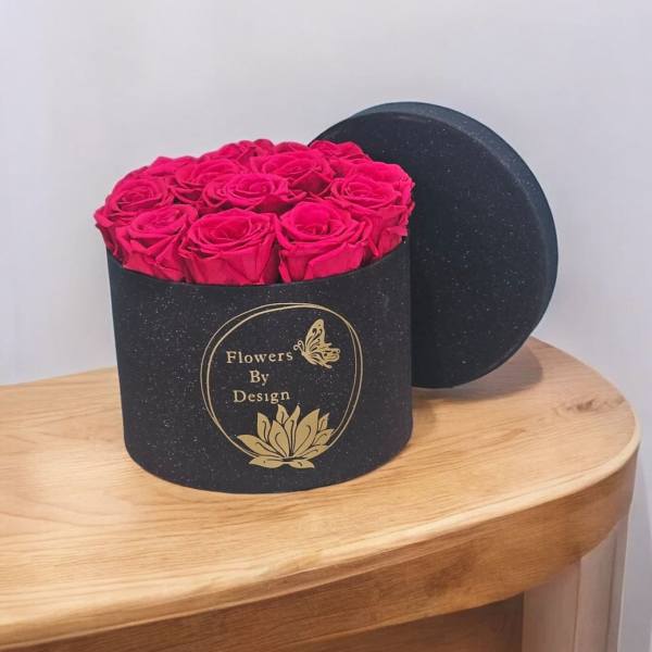 Pink roses in a black round gift box with a lid behind it