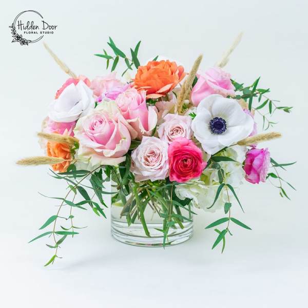 Mixed pink, white, and orange flowers arranged in a clear glass vase