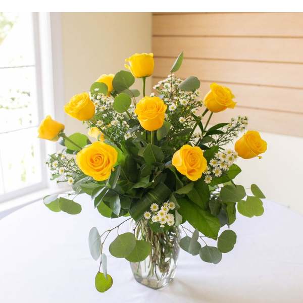 Yellow roses in a clear glass vase with small white filler flowers