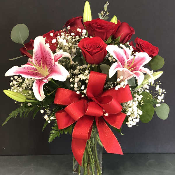 Arrangement of red roses and pink lilies with baby's breath in a clear vase with a large red bow