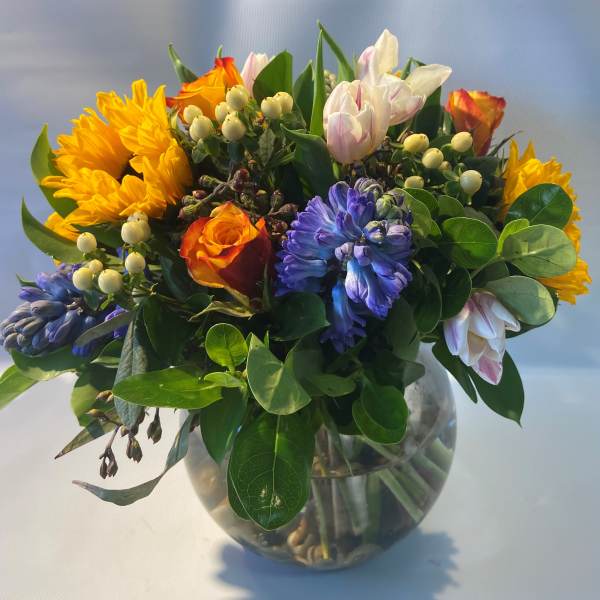Mixed bouquet of sunflowers, roses, tulips, and hyacinths in a glass vase