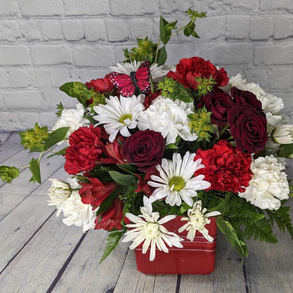 Red and white mixed bouquet in a red container with a butterfly pick