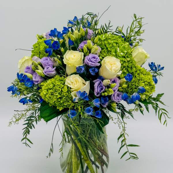 Bouquet of blue, lavender, and white flowers in a clear glass vase