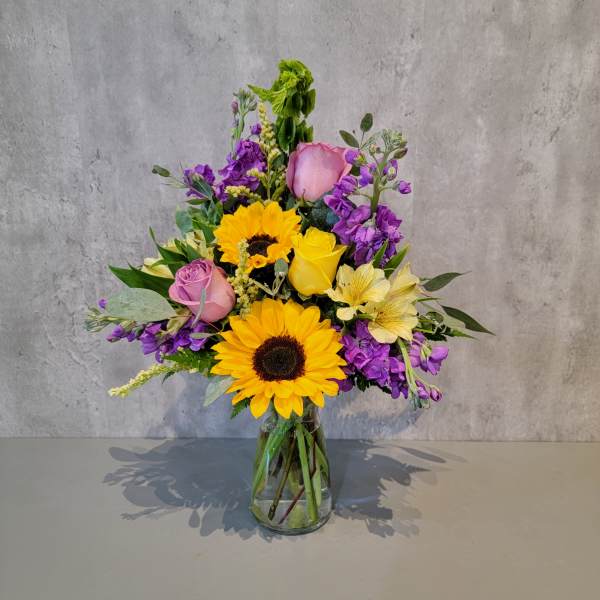Mixed bouquet of sunflowers, roses, and purple flowers in a glass vase