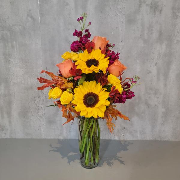 Tall bouquet of sunflowers, roses, and magenta flowers in a glass vase