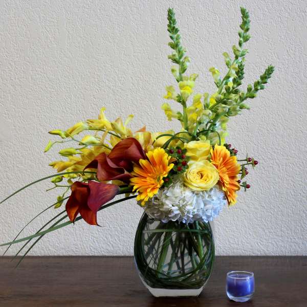 Yellow and orange floral arrangement in a glass vase with a blue candle nearby