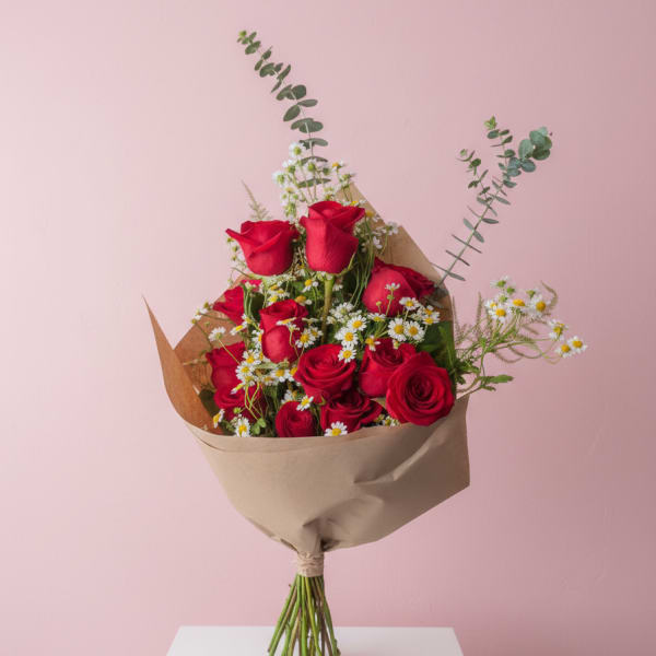 Bouquet of red roses and small white daisies wrapped in brown paper