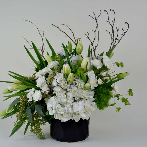 White floral arrangement in a black vase with tall branches and green accents