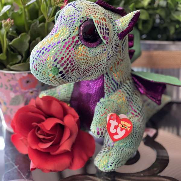 Plush dragon with a red rose and pink flowers in the background