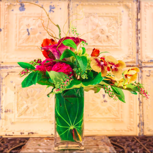 Tropical floral arrangement in a clear glass vase with orchids and calla lilies