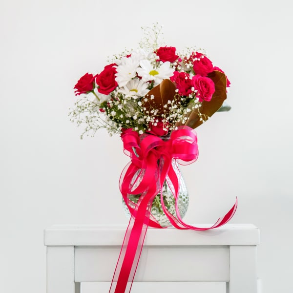Bouquet of red and white flowers in a glass vase with a pink ribbon