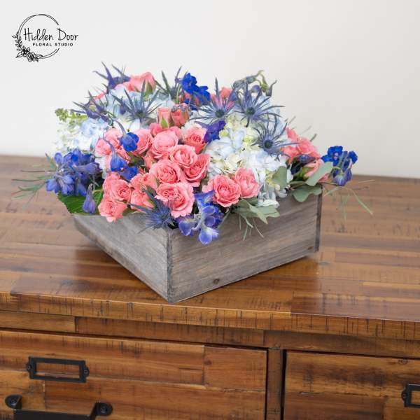 Pink and blue flowers arranged in a rustic wooden box