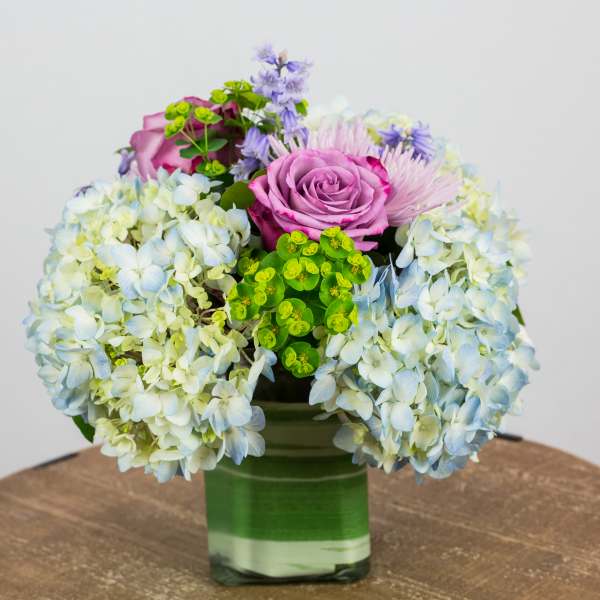 Pink roses and blue hydrangeas in a green glass vase
