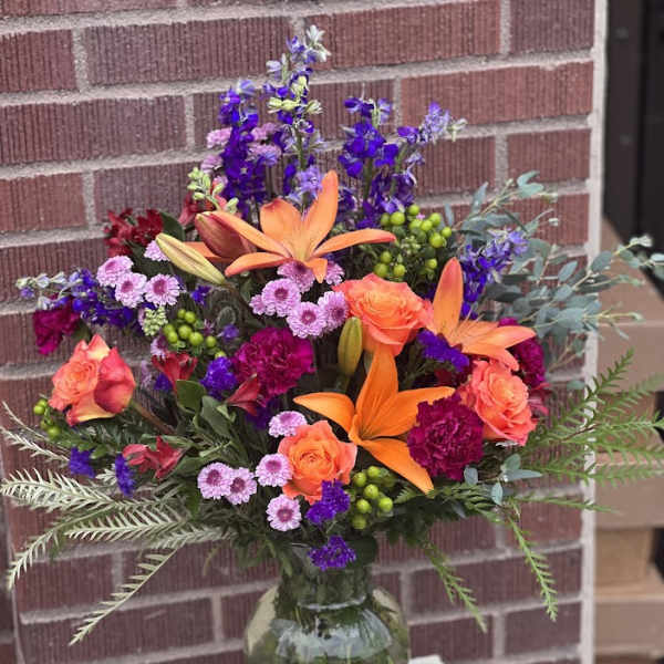 Bright mixed bouquet in a glass vase with orange lilies and roses