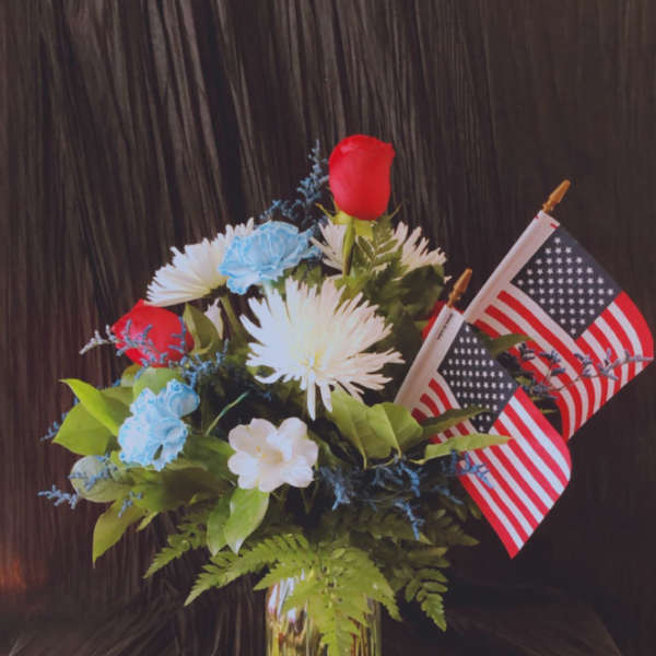 Bouquet of red, white, and blue flowers in a glass vase with two small American flags